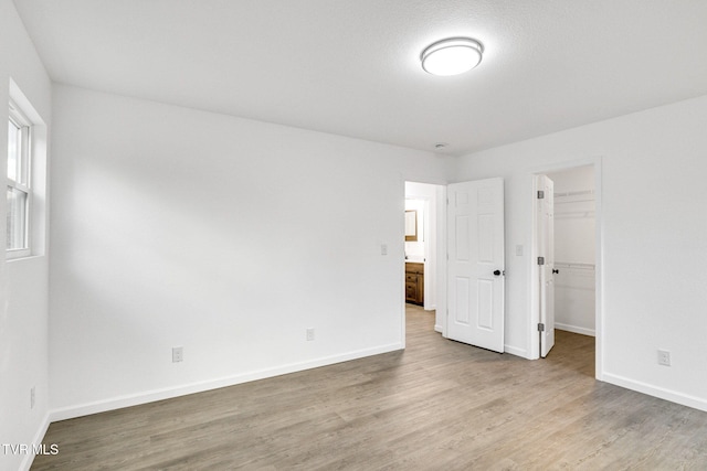 unfurnished bedroom featuring a closet, wood finished floors, a walk in closet, and baseboards