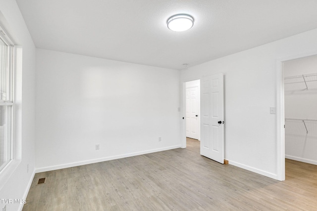 unfurnished bedroom with light wood-style floors, a walk in closet, a closet, and baseboards