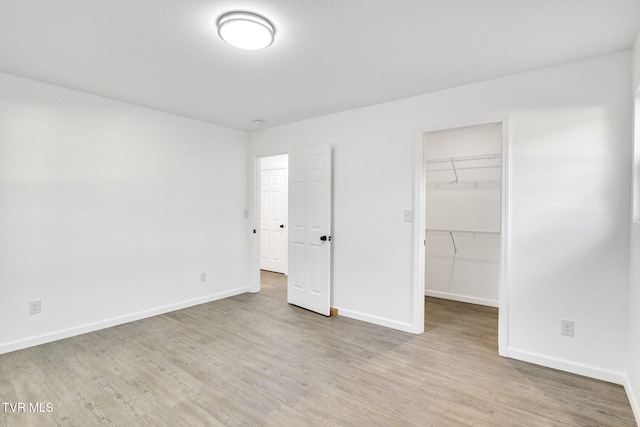 unfurnished bedroom featuring baseboards, a closet, a walk in closet, and light wood-style floors