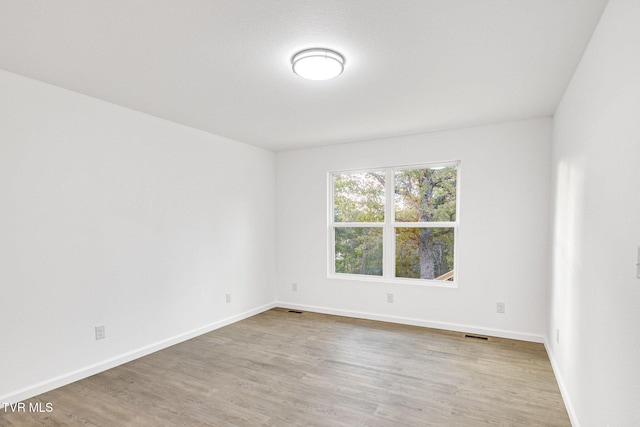 empty room with wood finished floors, visible vents, and baseboards