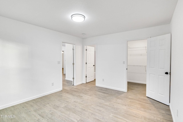 unfurnished bedroom with baseboards, a spacious closet, a closet, and light wood-style floors