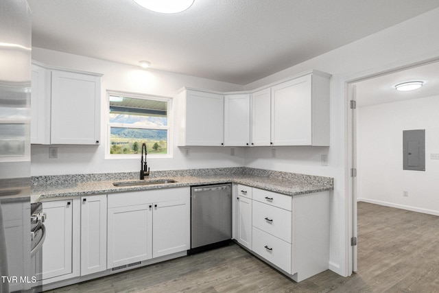 kitchen with stainless steel dishwasher, white cabinets, a sink, wood finished floors, and electric panel