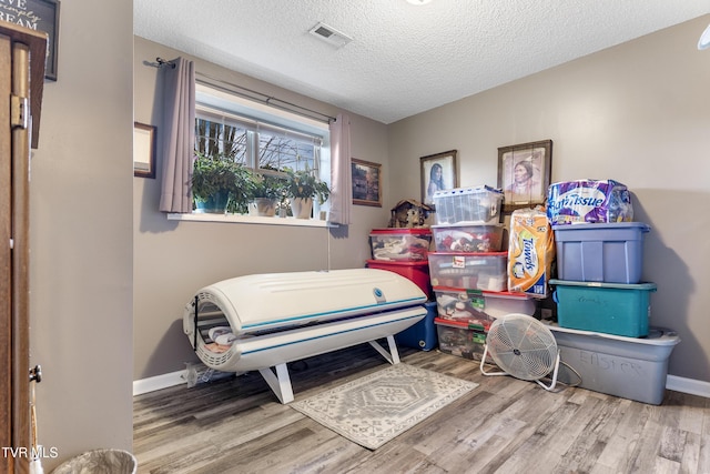 bedroom featuring a textured ceiling, wood finished floors, visible vents, and baseboards