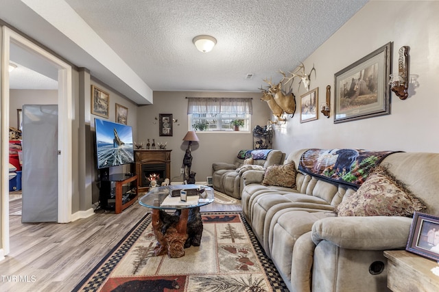 living room with a warm lit fireplace, a textured ceiling, baseboards, and wood finished floors