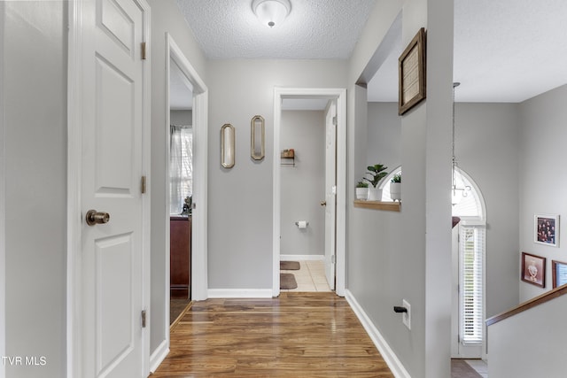 hall featuring a textured ceiling, baseboards, and wood finished floors