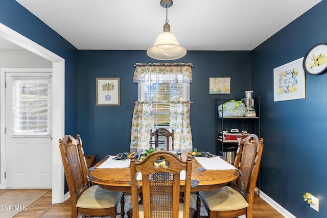 dining space featuring a textured ceiling, wood finished floors, and baseboards