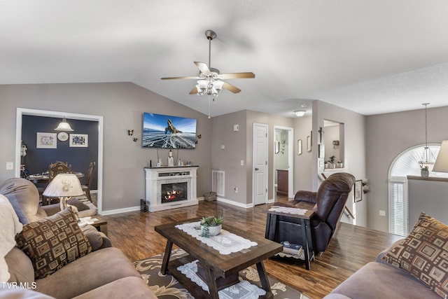 living area featuring a warm lit fireplace, wood finished floors, visible vents, baseboards, and vaulted ceiling