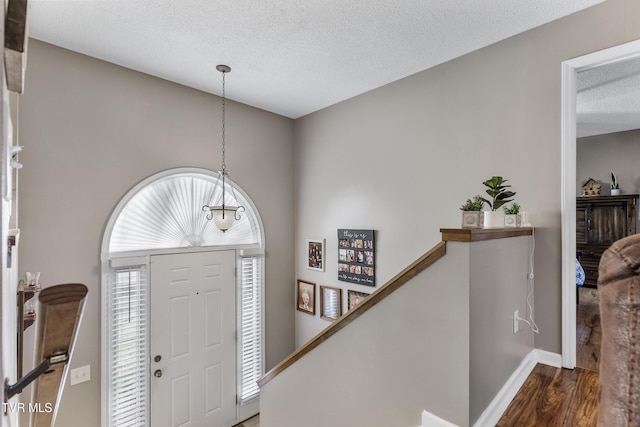 entryway with a textured ceiling, wood finished floors, and baseboards