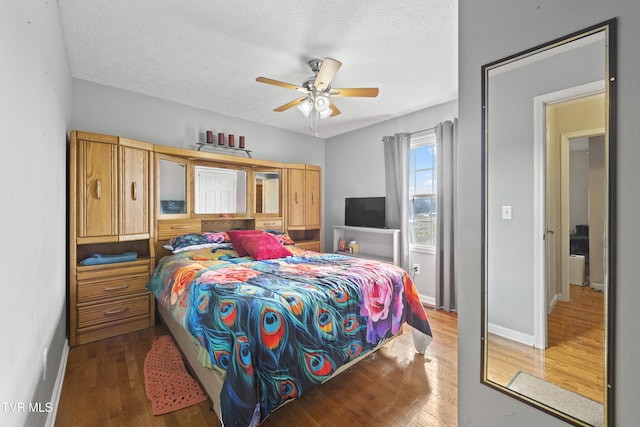 bedroom featuring a ceiling fan, a textured ceiling, baseboards, and wood finished floors