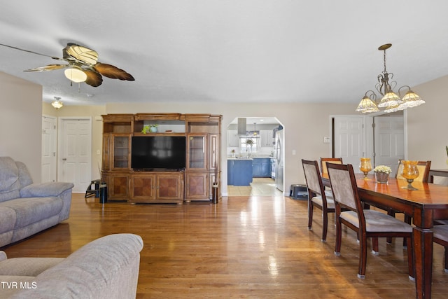 living room with arched walkways, ceiling fan with notable chandelier, and wood finished floors