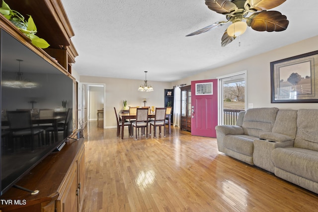 living area with a textured ceiling, ceiling fan with notable chandelier, wood finished floors, and baseboards