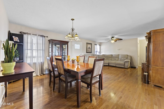 dining space featuring light wood-style floors, a textured ceiling, baseboards, and ceiling fan with notable chandelier