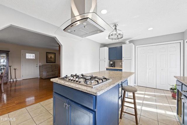 kitchen with arched walkways, a kitchen island, blue cabinets, island exhaust hood, and stainless steel gas stovetop