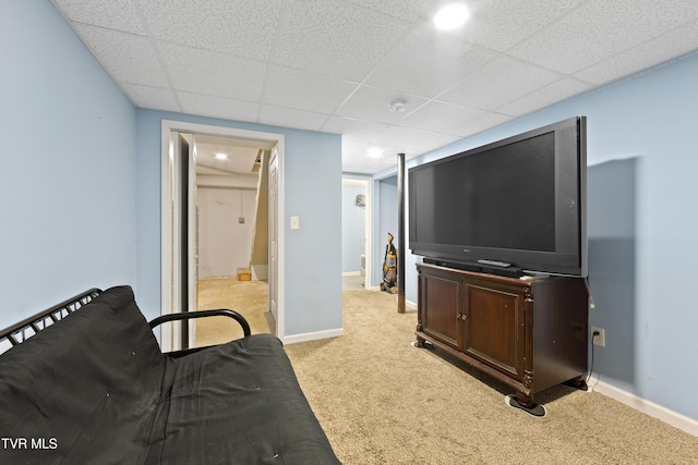 living area with baseboards, a drop ceiling, and light colored carpet