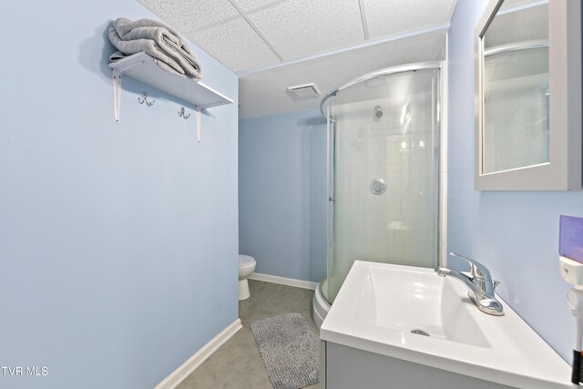 full bath featuring a drop ceiling, toilet, vanity, baseboards, and a stall shower