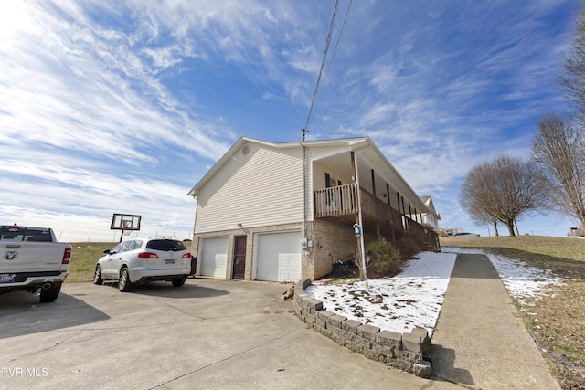 view of side of home with driveway, brick siding, an attached garage, and a balcony