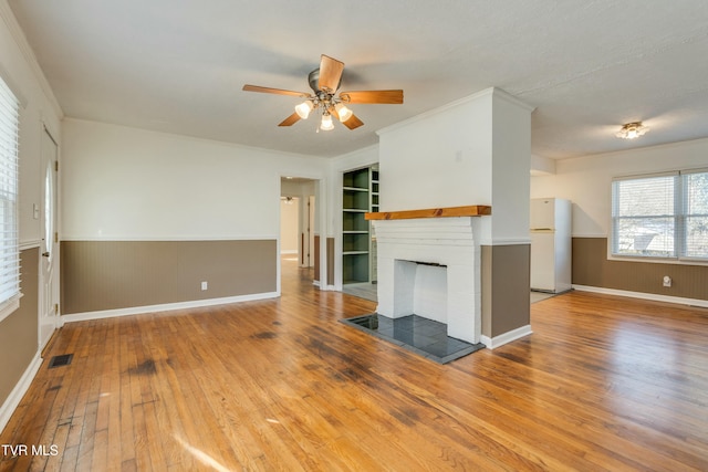 unfurnished living room featuring ceiling fan, a wainscoted wall, wood finished floors, visible vents, and a brick fireplace