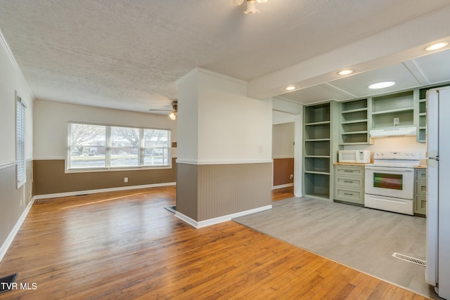 kitchen with under cabinet range hood, white appliances, wainscoting, open shelves, and green cabinetry