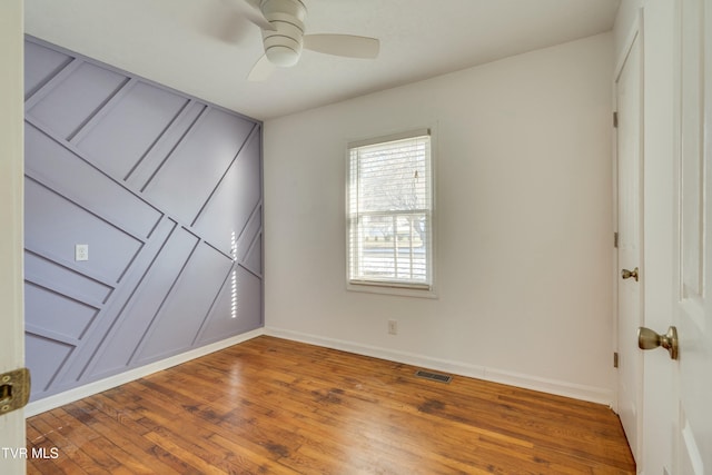 spare room with a ceiling fan, visible vents, baseboards, and wood finished floors