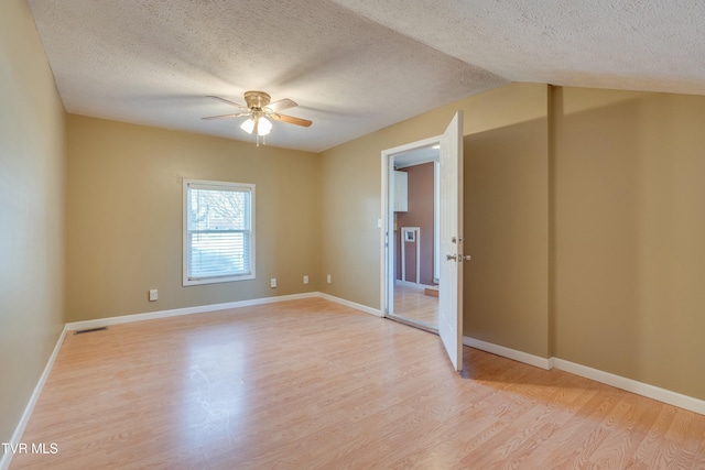 spare room featuring baseboards, visible vents, a ceiling fan, light wood-style flooring, and a textured ceiling