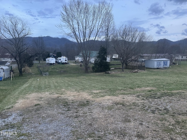 view of yard with a storage shed, an outbuilding, fence, and a mountain view