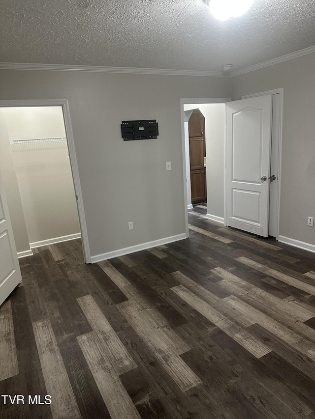 empty room featuring a textured ceiling, dark wood-style flooring, baseboards, and crown molding