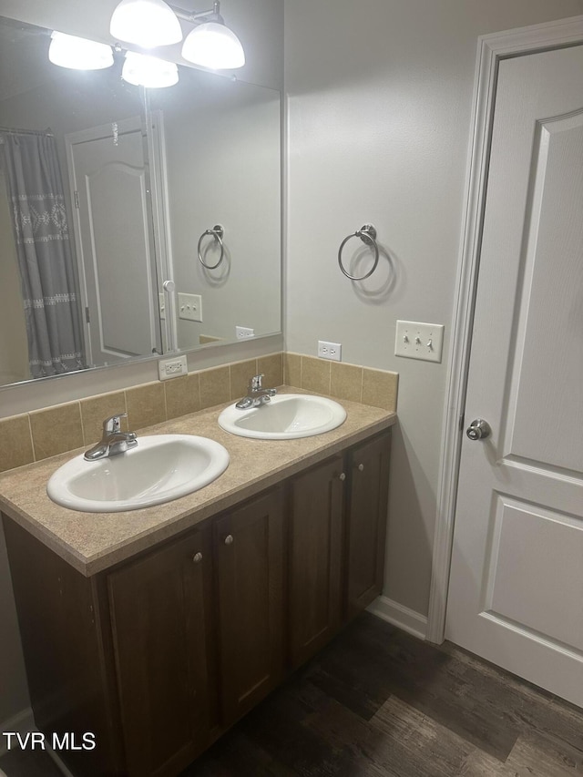 full bathroom featuring wood finished floors, a sink, backsplash, and double vanity