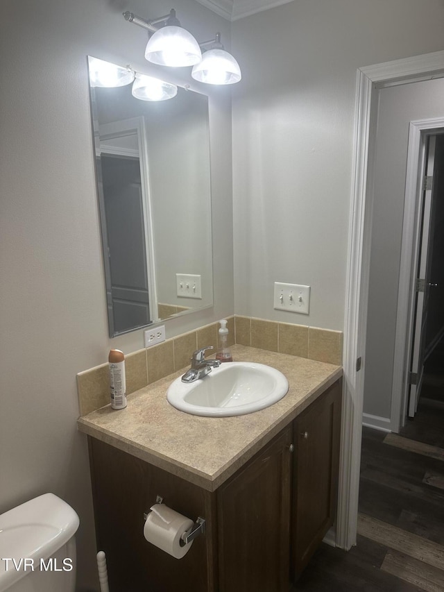 half bath with toilet, wood finished floors, and vanity