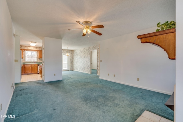 unfurnished living room with light carpet, wallpapered walls, baseboards, ceiling fan, and a textured ceiling