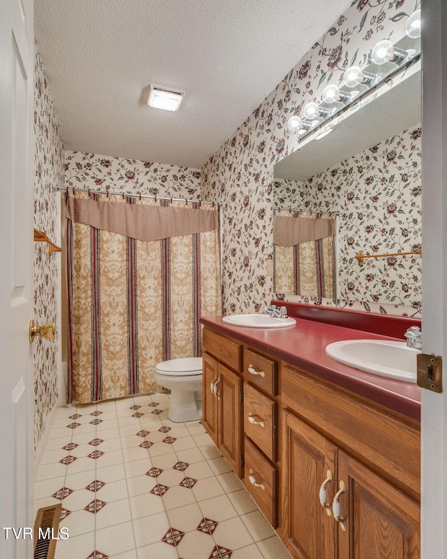 bathroom featuring a sink, wallpapered walls, double vanity, and a textured ceiling