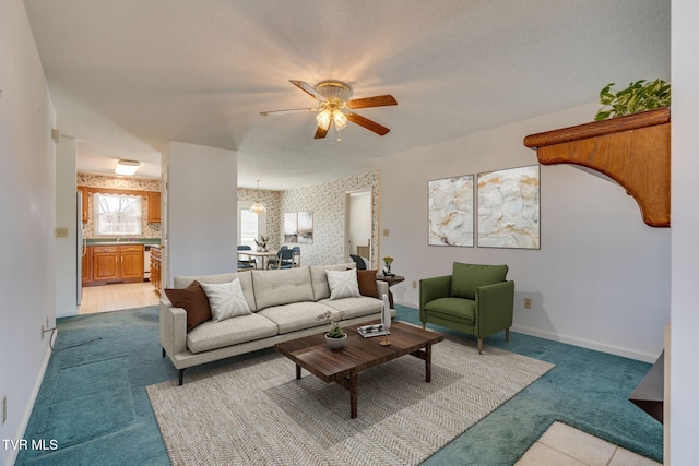 living room with a textured ceiling, light colored carpet, a ceiling fan, baseboards, and wallpapered walls