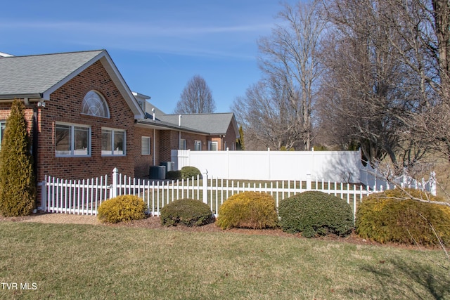 view of side of home with roof with shingles, brick siding, central air condition unit, a lawn, and fence