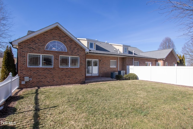 rear view of house featuring cooling unit, brick siding, a yard, and a fenced backyard