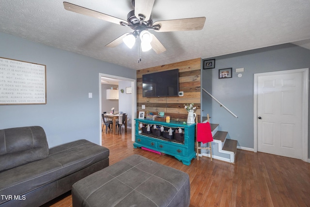 living room featuring stairway, wood walls, ceiling fan, a textured ceiling, and wood finished floors