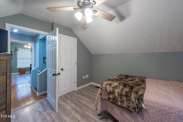 bedroom featuring lofted ceiling, baseboards, a textured ceiling, and light wood finished floors