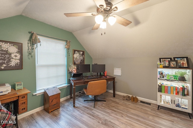 office area with a textured ceiling, lofted ceiling, light wood-style flooring, visible vents, and baseboards