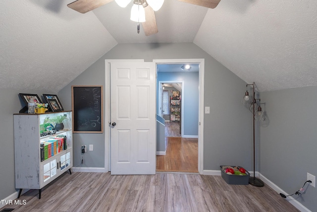 additional living space with baseboards, a ceiling fan, lofted ceiling, light wood-style flooring, and a textured ceiling