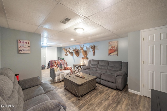 living room with a drop ceiling, visible vents, baseboards, and wood finished floors