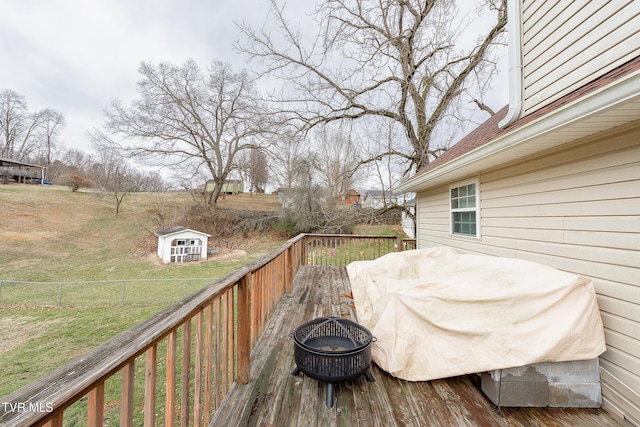 wooden terrace featuring a fire pit, a storage shed, an outbuilding, and fence