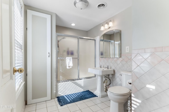 bathroom featuring tile walls, bath / shower combo with glass door, visible vents, toilet, and tile patterned flooring