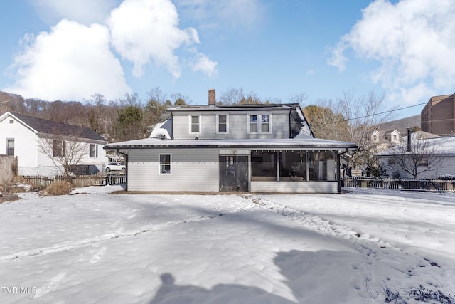 snow covered property with a sunroom, fence, and a chimney