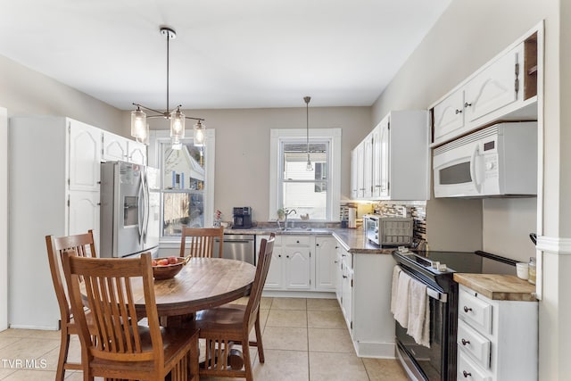 kitchen with light tile patterned floors, dark countertops, stainless steel appliances, white cabinetry, and pendant lighting