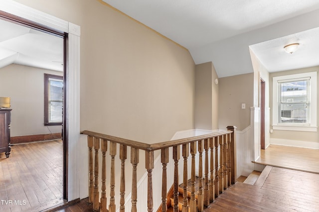 hall featuring lofted ceiling, baseboards, wood finished floors, and an upstairs landing