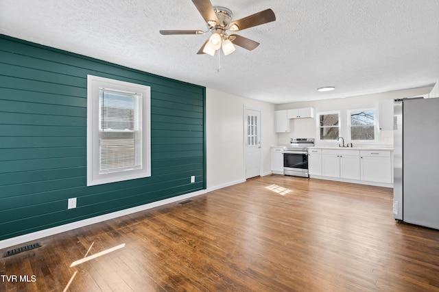 unfurnished living room with baseboards, visible vents, wood finished floors, a textured ceiling, and a sink