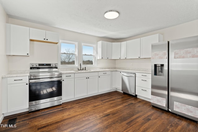 kitchen featuring a textured ceiling, stainless steel appliances, dark wood-style flooring, a sink, and white cabinets