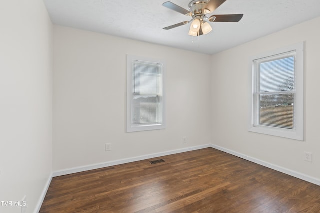 spare room featuring dark wood-style flooring, plenty of natural light, and visible vents