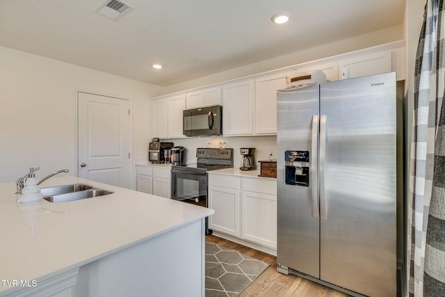 kitchen featuring wood finished floors, a sink, visible vents, white cabinetry, and black appliances