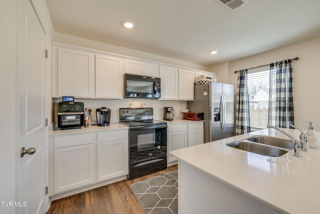 kitchen with dark wood-style flooring, a sink, visible vents, white cabinets, and black appliances