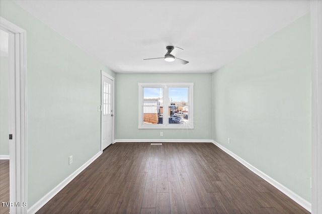 unfurnished room featuring dark wood-type flooring, a ceiling fan, and baseboards