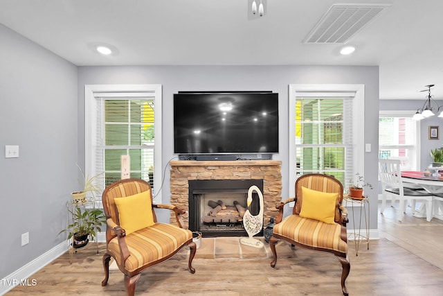 living area featuring a stone fireplace, light wood-style flooring, recessed lighting, visible vents, and baseboards